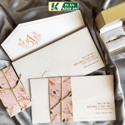 Thiết kế nổi bật với tông kem ngà phối hồng phấn và họa tiết hoa lá nhẹ nhàng, kết hợp thiệp túi cùng đai quấn dây mộc tạo cảm giác tinh tế.