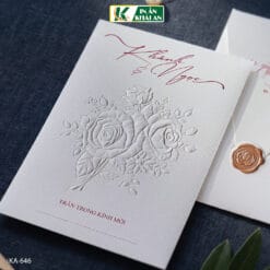 Mẫu thiệp cưới sử dụng nền trắng kết hợp chữ đỏ trầm, tạo tổng thể thanh lịch và dễ đọc. Thiết kế theo hướng hiện đại, nổi bật với họa tiết hoa được dập nổi trên bề mặt cùng bố cục thoáng.